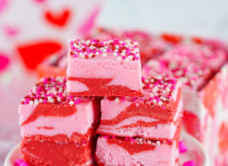 Square pieces of pink and red swirled Valentine Fudge, topped with colorful sprinkles, arranged on a plate.