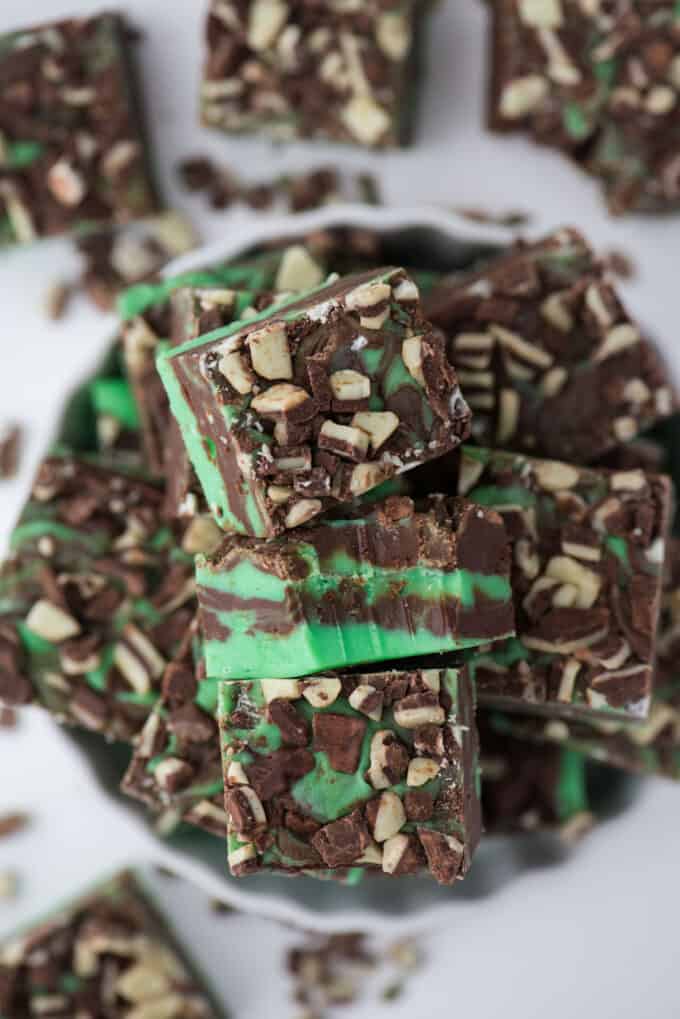 Stack of chocolate mint fudge pieces from homemade fudge recipes, topped with crushed nuts on a plate.