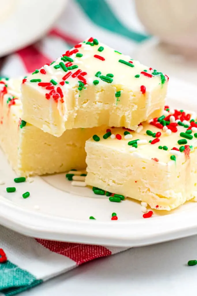 Two pieces of homemade fudge with red and green sprinkles are stacked on a white plate, showcasing delightful results from cherished family recipes.