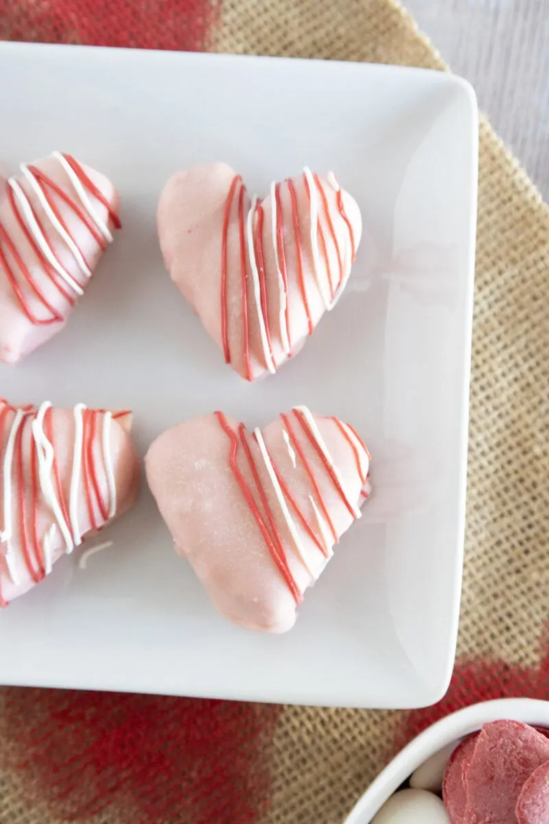 Heart-shaped pastries with pink icing and red and white drizzle are placed on a white plate.