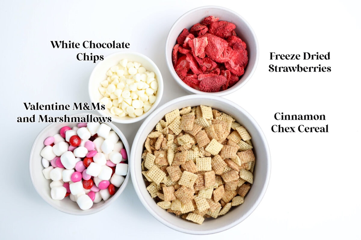 Bowls with ingredients: white chocolate chips, freeze-dried strawberries, Valentine M&Ms and marshmallows, and Cinnamon Chex cereal.