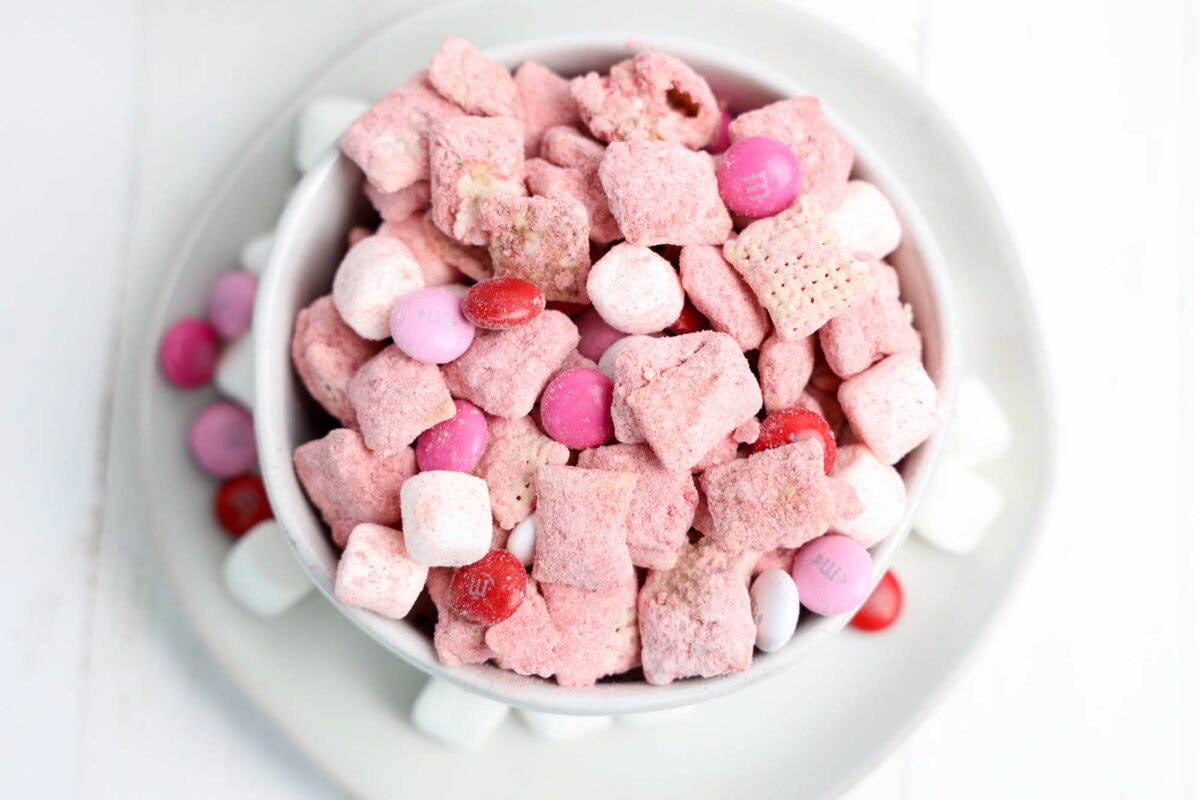 A white bowl filled with pink and white cereal, candy-coated chocolates, and marshmallows on a white plate.