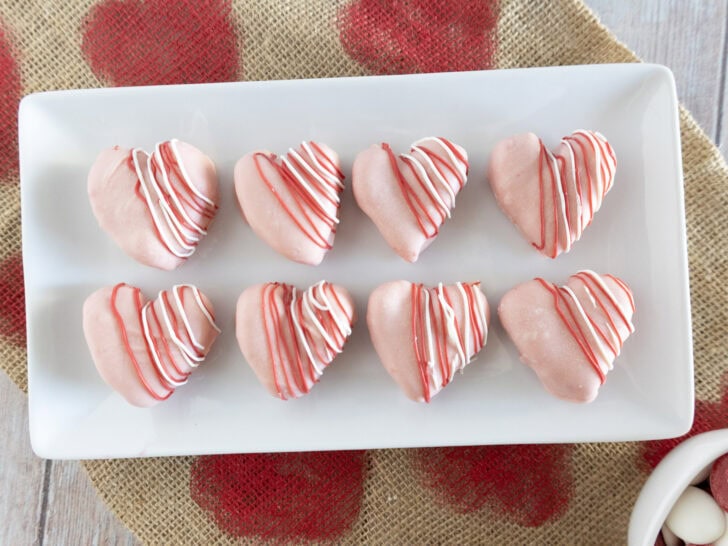 Heart-shaped cookies drizzled with pink and red icing are arranged on a white rectangular plate.