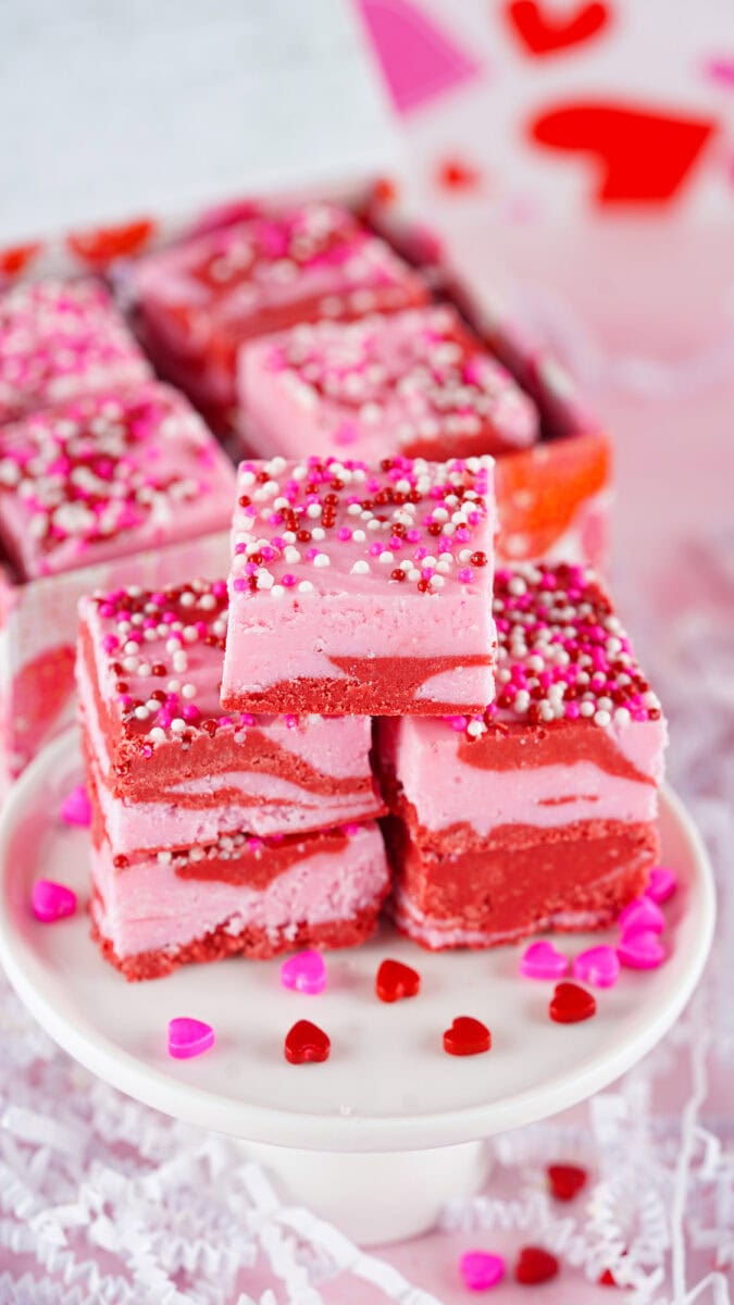 Pink and red marbled fudge squares stacked on a plate, topped with heart-shaped and round sprinkles.