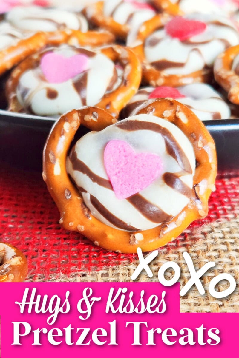 Close-up of pretzel treats adorned with chocolate, a pink heart candy, and "Hugs & Kisses Pretzel Treats" text at the bottom. The heartwarming display sits on a red textured surface, embodying the message of hugs and kisses.