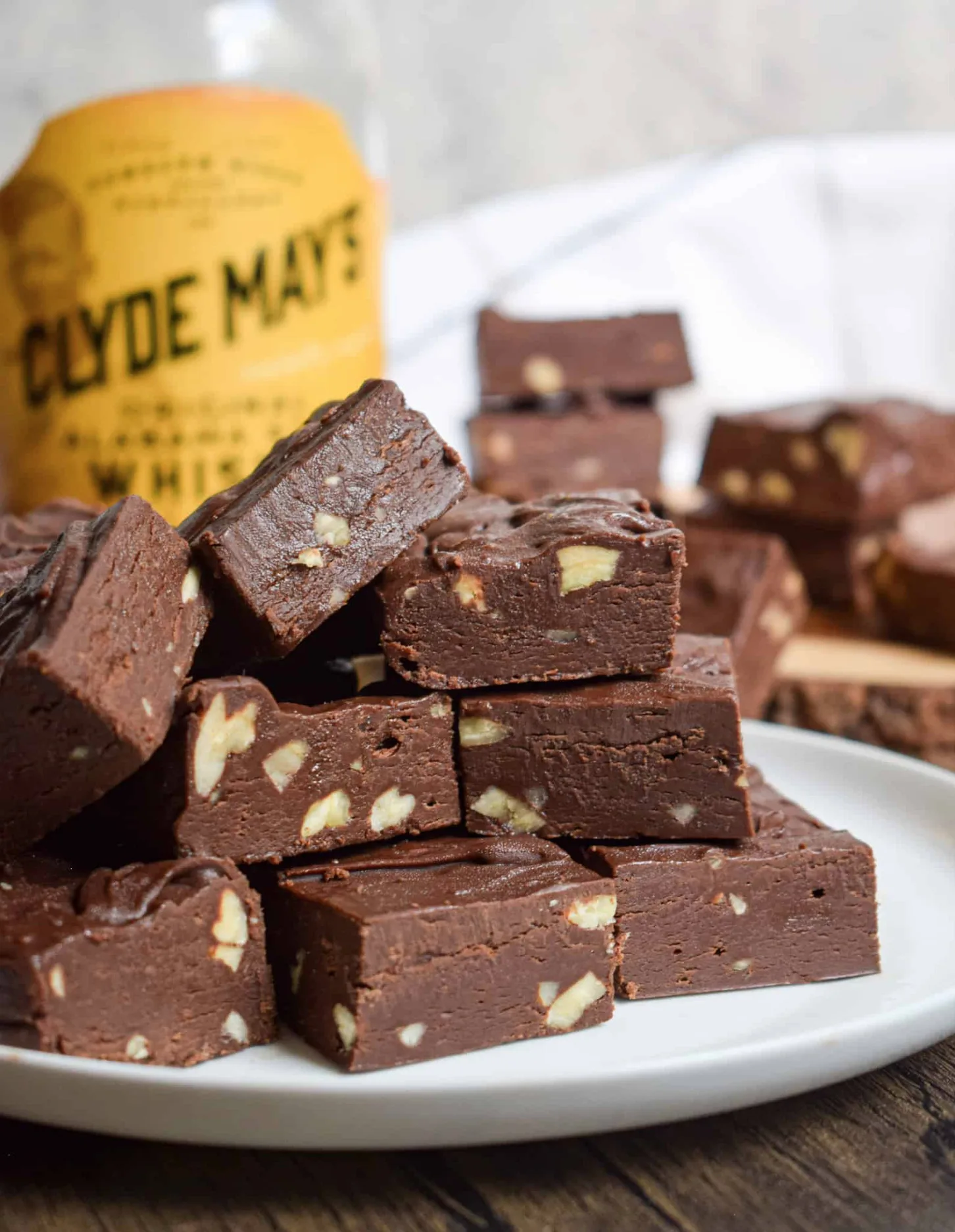 A plate of chocolate fudge with nuts, inspired by homemade fudge recipes, is stacked in front of a bottle labeled "Clyde May's.