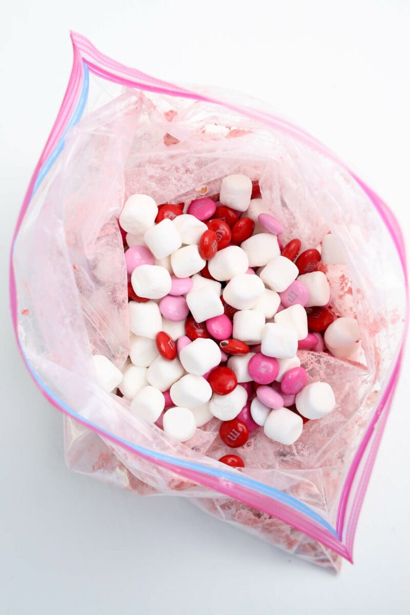 A clear zip-lock bag containing red and pink chocolates mixed with white marshmallows.