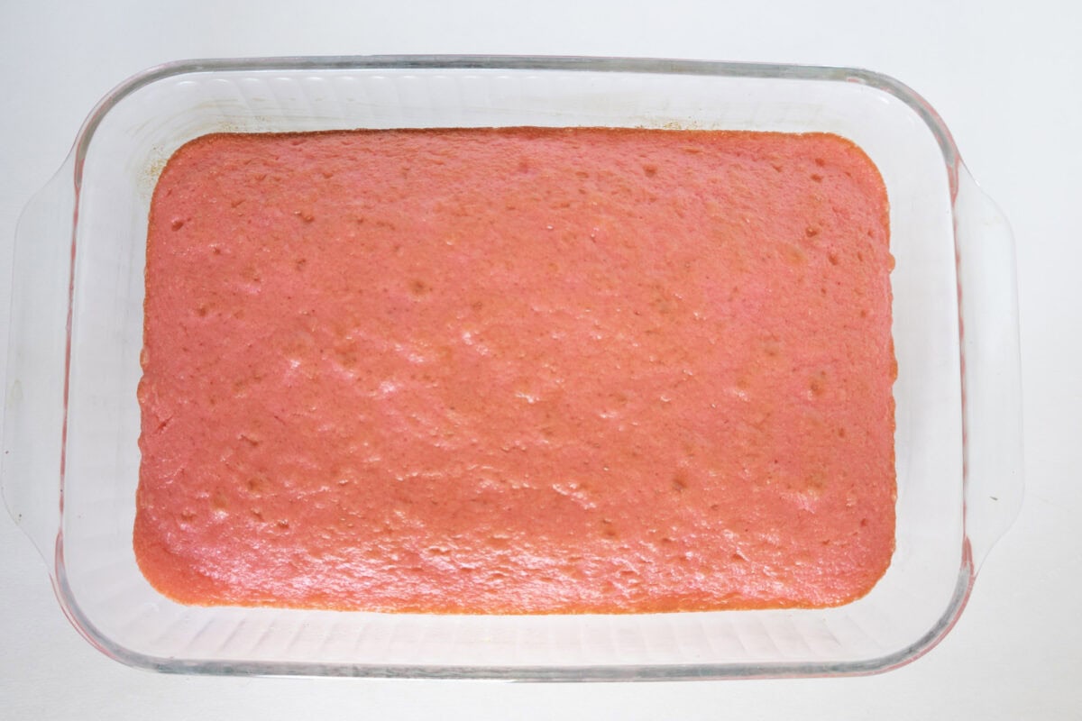 A rectangular glass baking dish with a pink cake inside, viewed from above on a white surface.