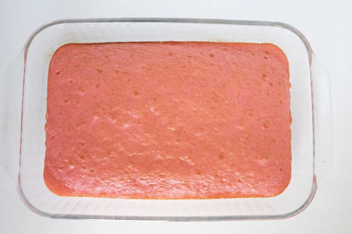 A rectangular glass baking dish with a pink cake inside, viewed from above on a white surface.