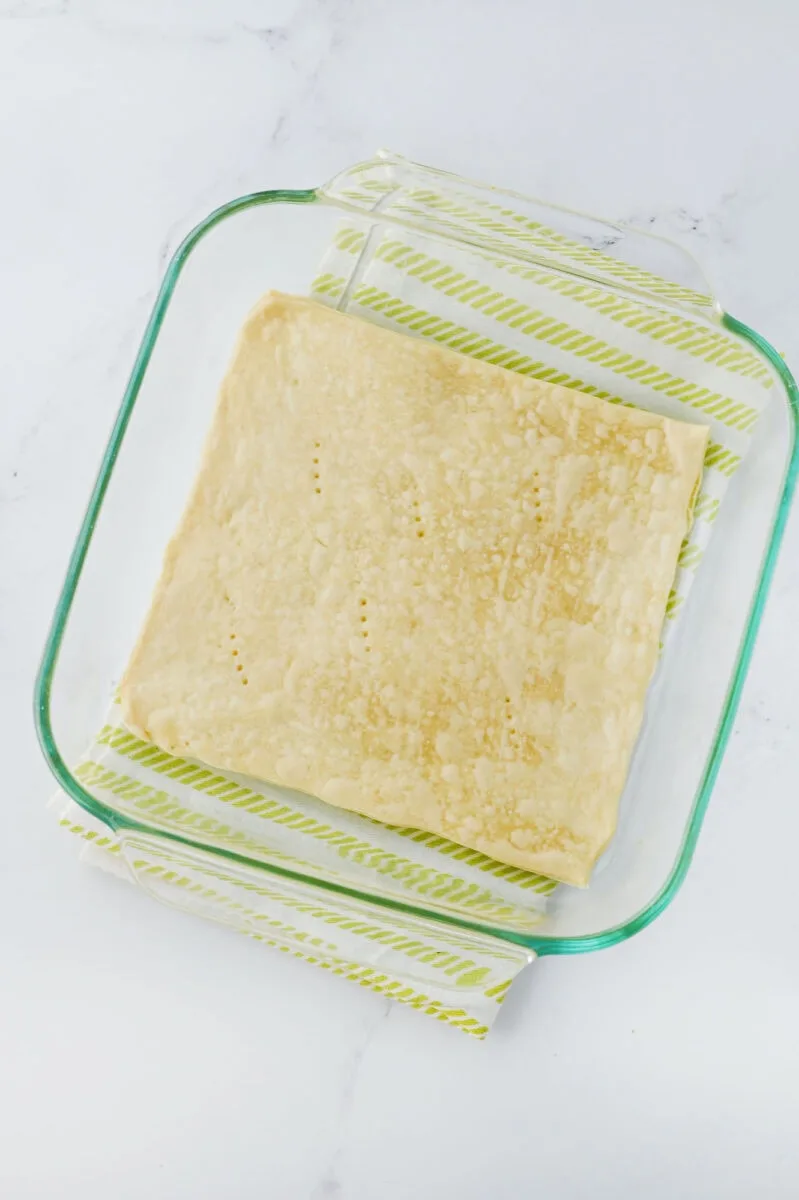 A glass baking dish cradles a rectangular piece of dough, lightly textured, resting on a striped green and white towel—a perfect base for transforming into pecan pie fudge.