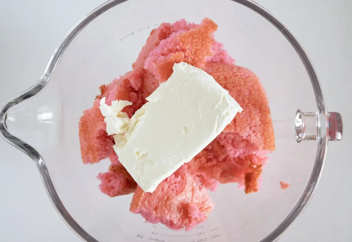 A bowl with pieces of pink cake and a block of cream cheese.