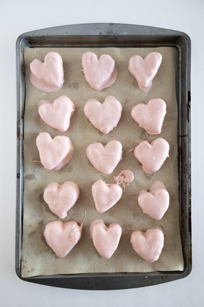 Heart-shaped, pink-frosted treats arranged on a parchment-lined baking tray.