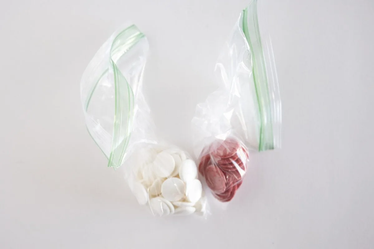 Two clear plastic bags contain white and red circular tokens on a white background.