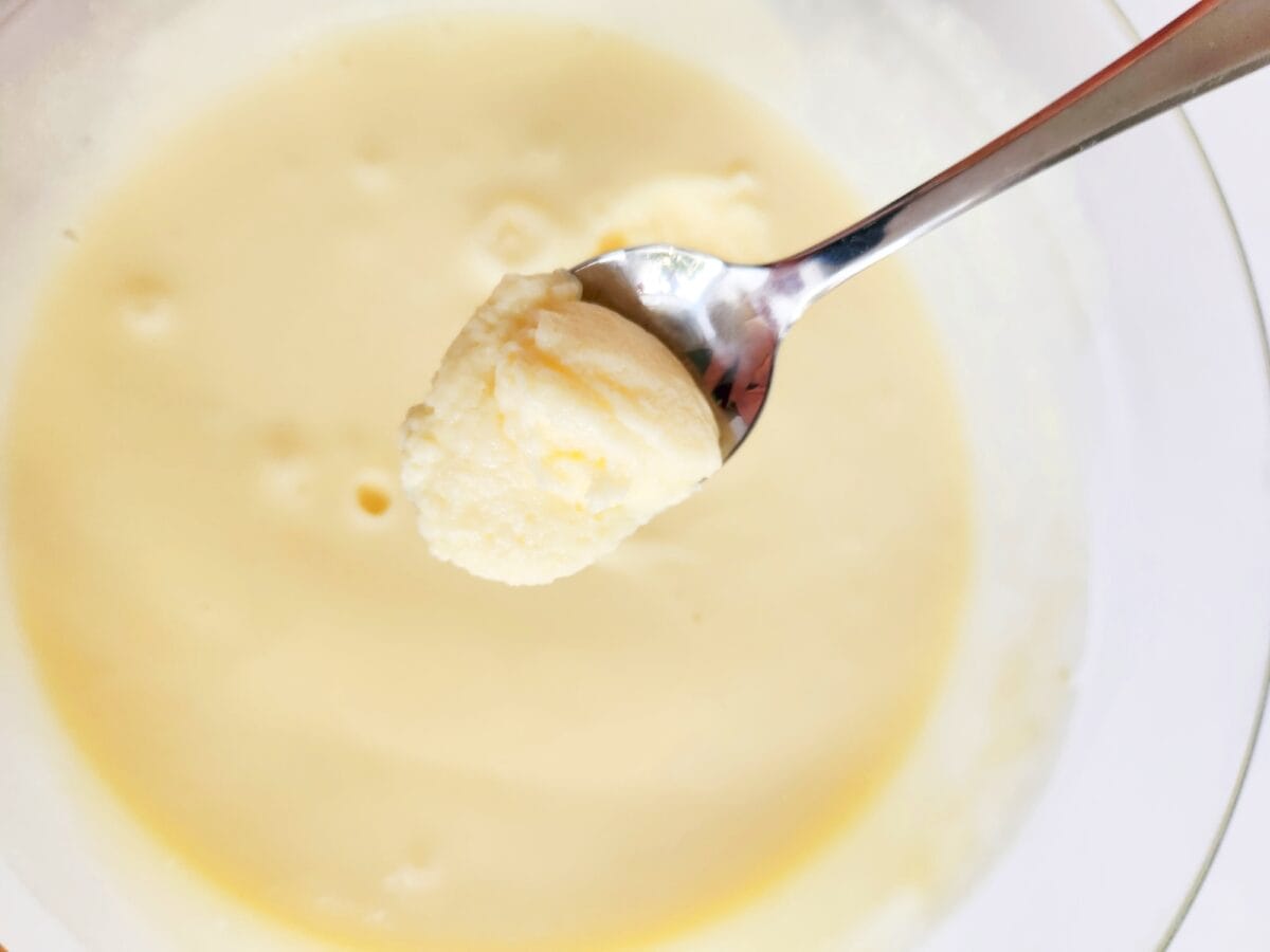 A spoonful of creamy, light yellow mashed potatoes is held above a bowl filled with more of the same.