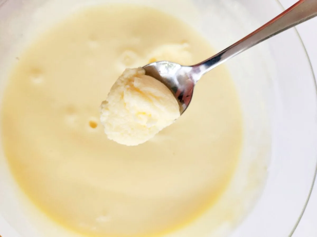 A spoonful of creamy, light yellow mashed potatoes is held above a bowl filled with more of the same.