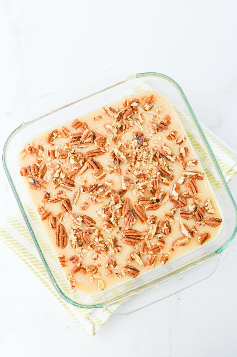 A glass baking dish cradles a delightful pecan pie fudge dessert, possibly a praline or cake, resting elegantly on a striped napkin.