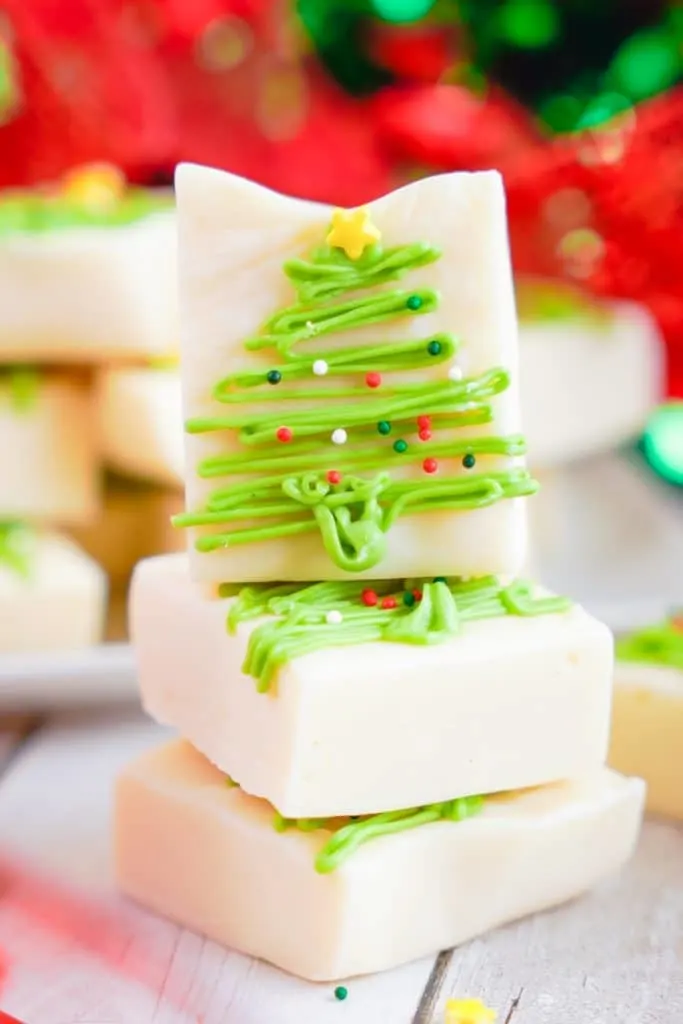 A stack of homemade fudge squares, beautifully decorated with green icing in the shape of Christmas trees, topped with a yellow star and sprinkles.