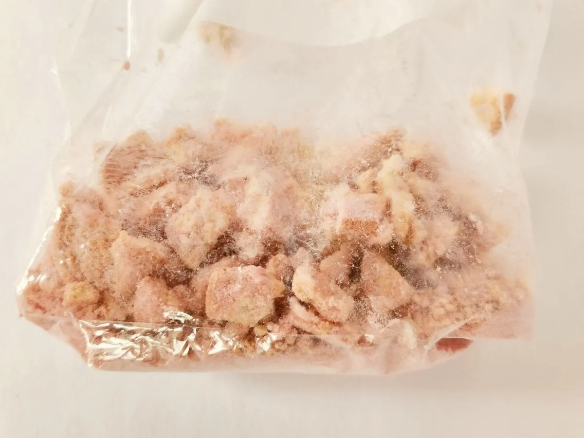 A clear plastic bag containing frosty, diced pink and beige pieces, likely frozen food, on a light surface.