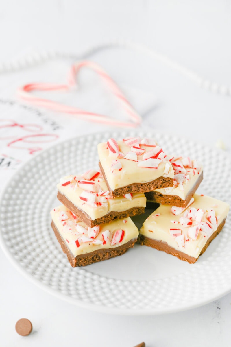 A plate of peppermint bark with crushed candy cane topping, stacked in neat rows on a white textured dish.