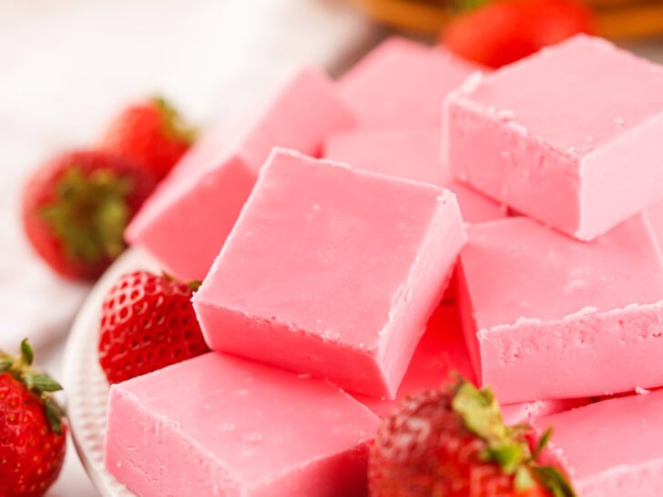 A plate of pink fudge squares with fresh strawberries placed around them.