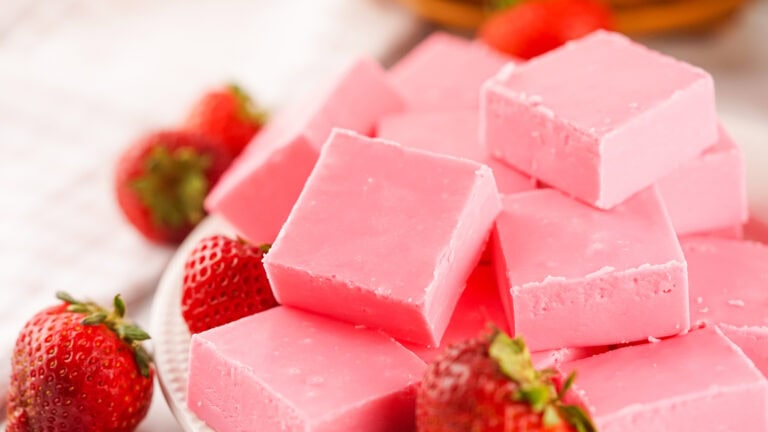 A plate of pink fudge squares with fresh strawberries placed around them.