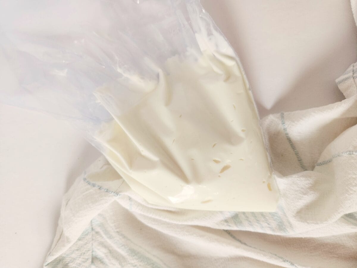 A clear plastic bag filled with a creamy white substance, placed on a white and light striped cloth.