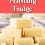 A stack of vanilla frosting fudge squares is placed on a wooden board, with white chips scattered around. The image is titled "2-Ingredient Frosting Fudge.