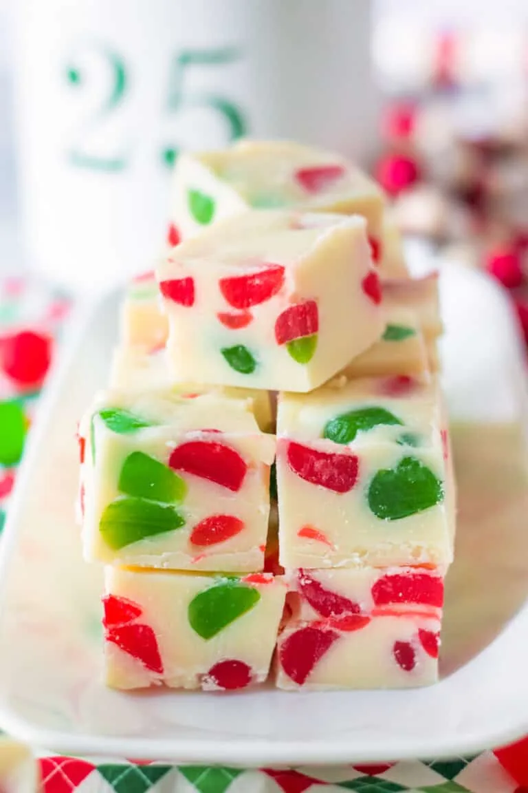 white fudge cubes, adorned with festive red and green candy pieces, stacked elegantly on a white plate.