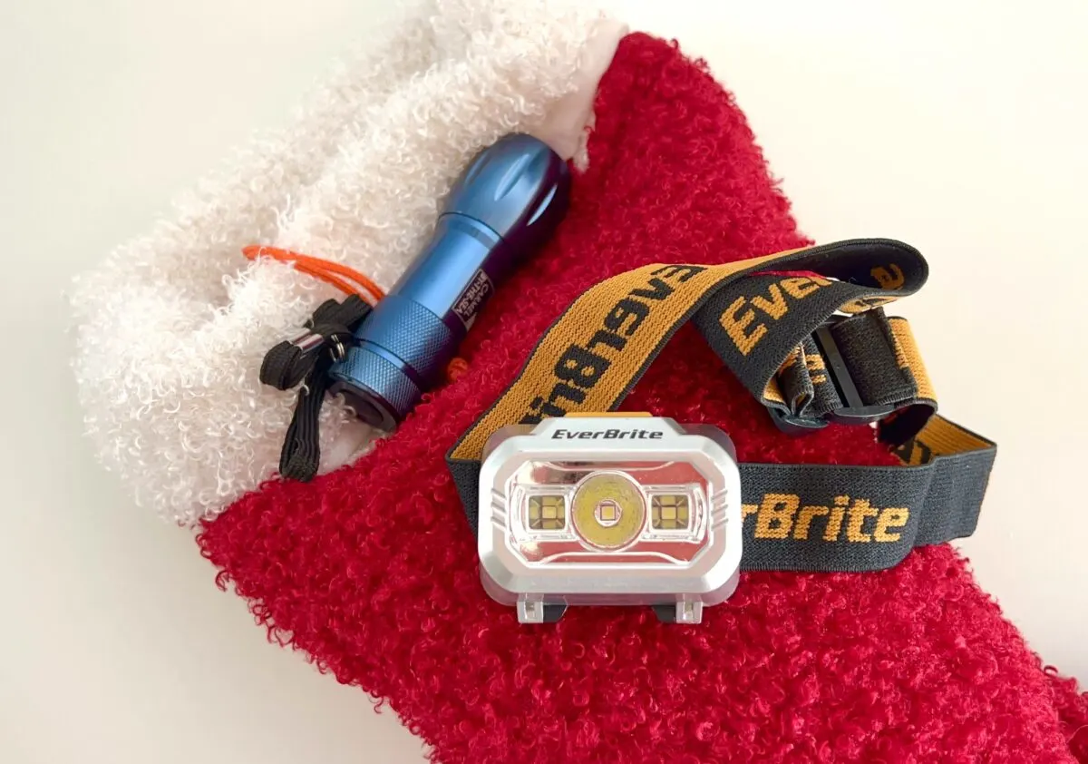 A red stocking contains a blue flashlight and an EverBrite headlamp with a yellow and black strap.