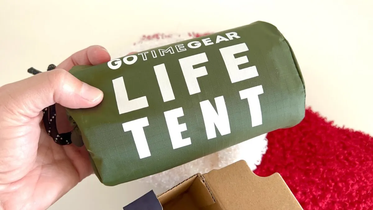 A hand holds a packaged green Go Time Gear Life Tent.