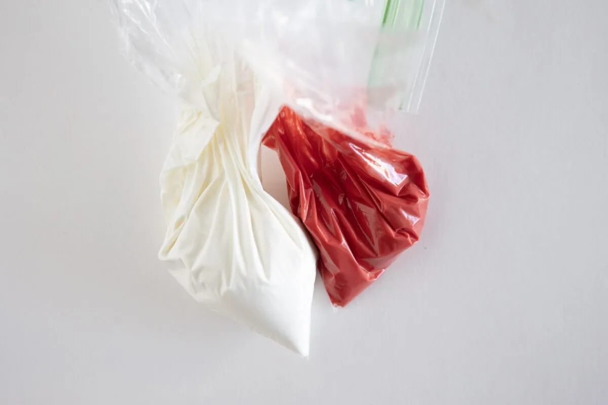 Two plastic bags on a white surface, one with white liquid and the other with red liquid, tied at the top.