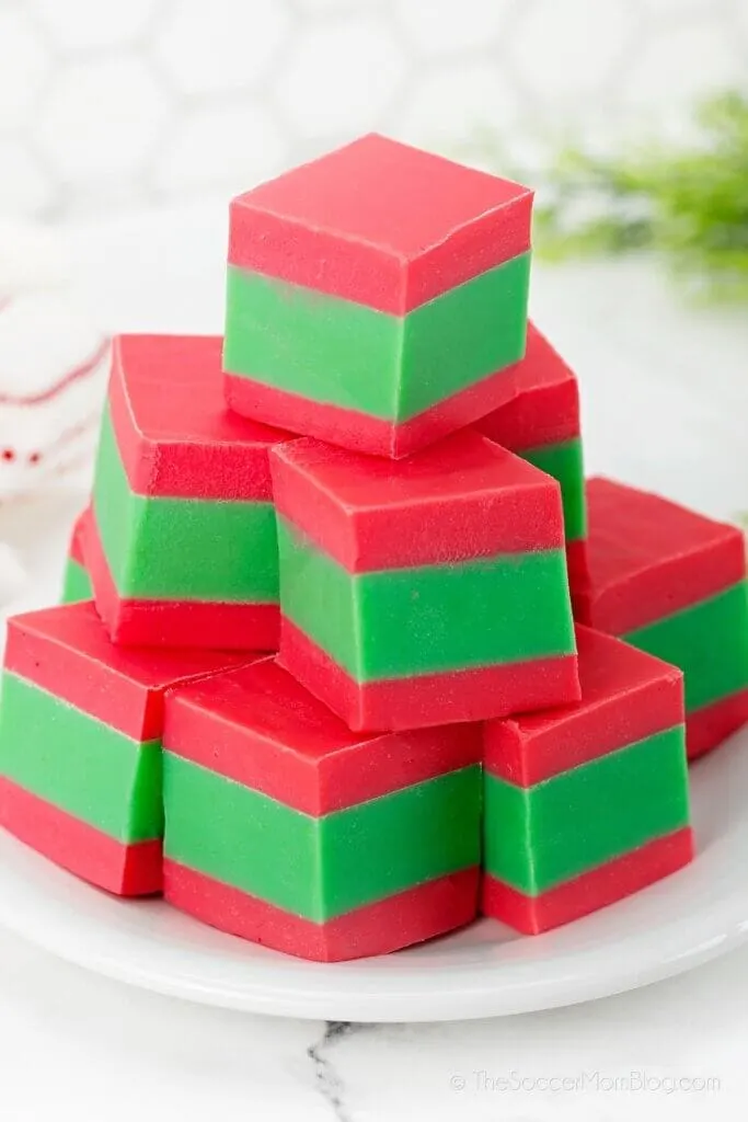 A stack of red and green layered fudge squares, crafted from cherished homemade fudge recipes, rests invitingly on a white plate.