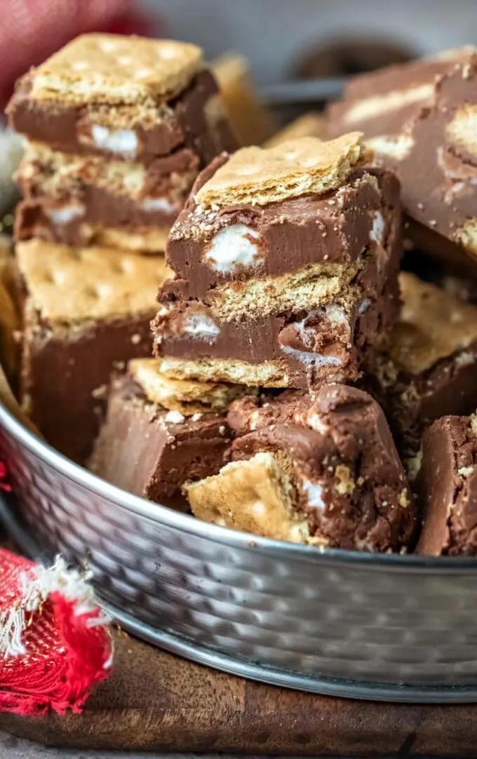 Stacked chocolate fudge pieces with marshmallow and graham cracker layers sit enticingly in a metal bowl, showcasing one of the finest homemade fudge recipes.