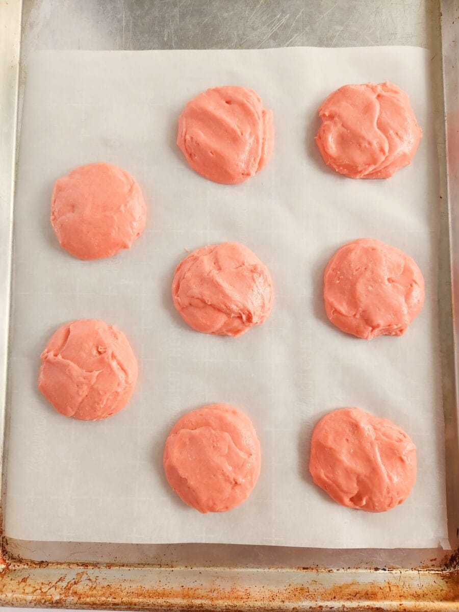 Nine pink cookie dough portions arranged on parchment paper on a baking tray.