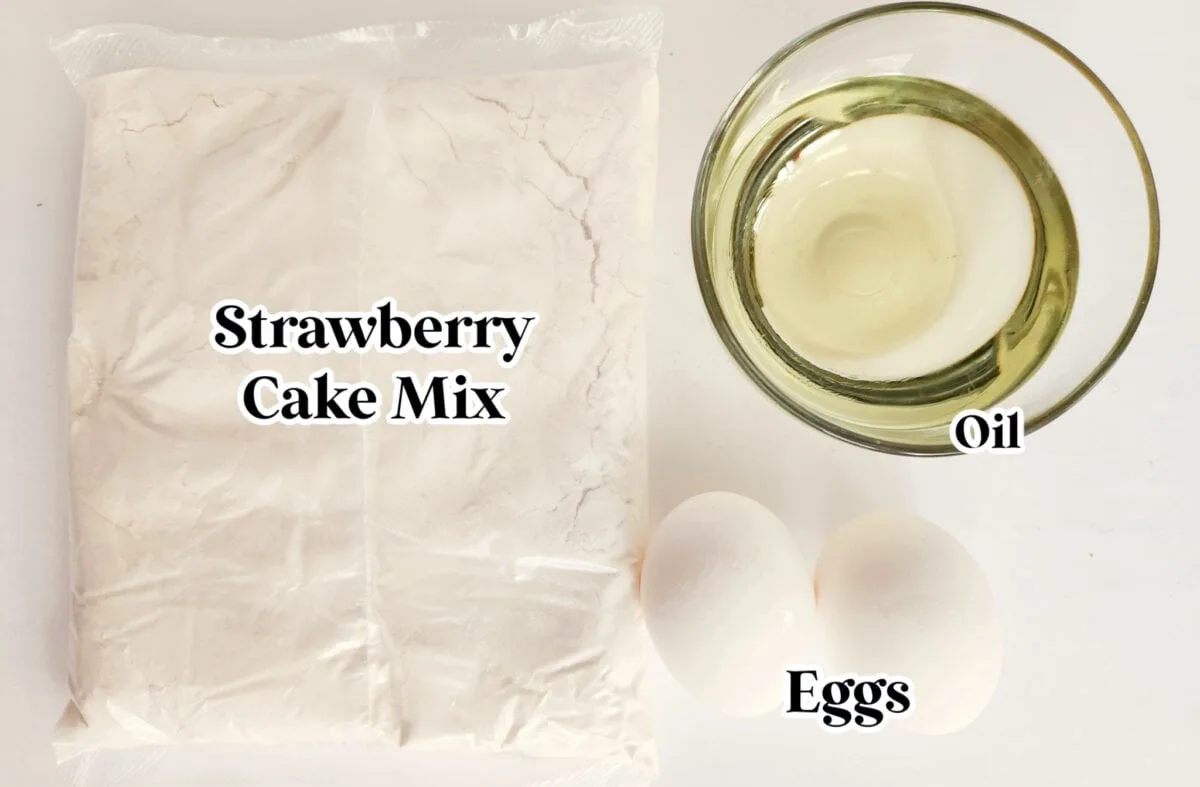 Ingredients for a cake: a sealed bag of strawberry cake mix, a clear bowl of oil, and two eggs on a white surface.