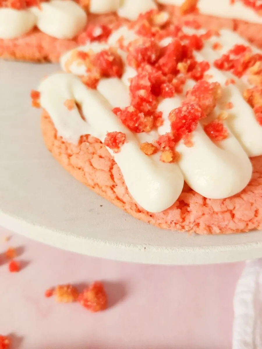 Close-up of pink cookies with white frosting and pink crumbs on a white plate.