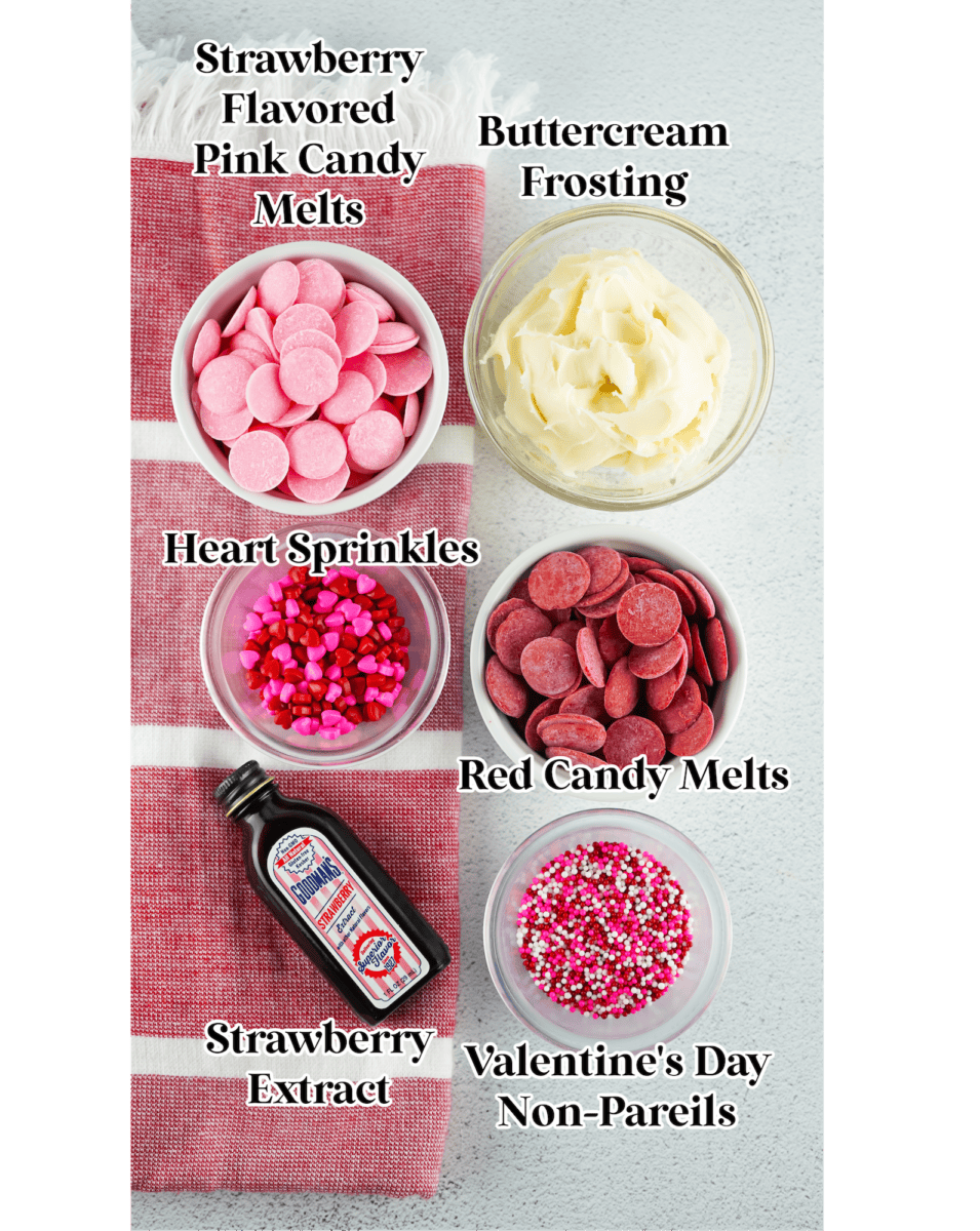 Various baking ingredients including strawberry flavored pink candy melts, buttercream frosting, heart sprinkles, red candy melts, strawberry extract, and Valentine's Day nonpareils are perfect for creating delightful Valentine Fudge.