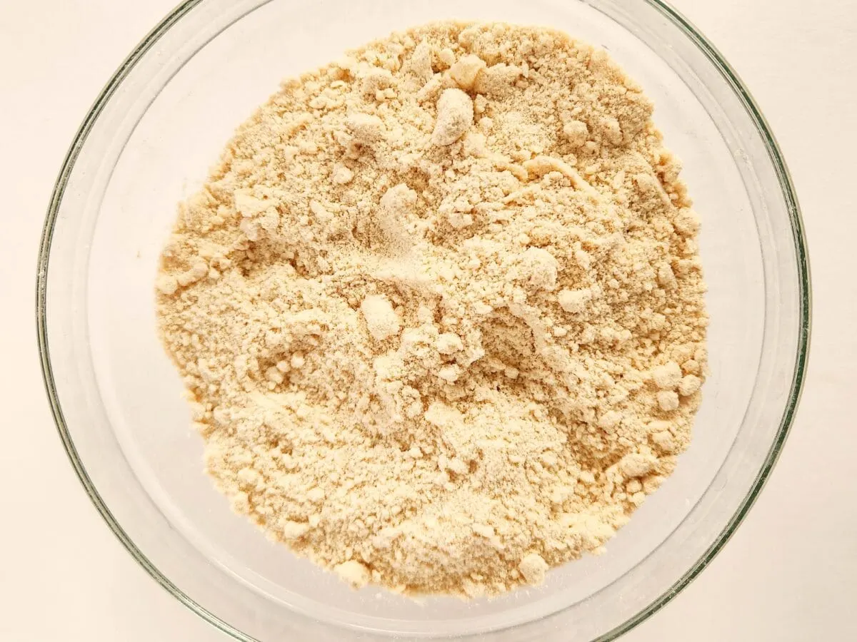 A glass bowl filled with finely ground almond flour on a white surface.