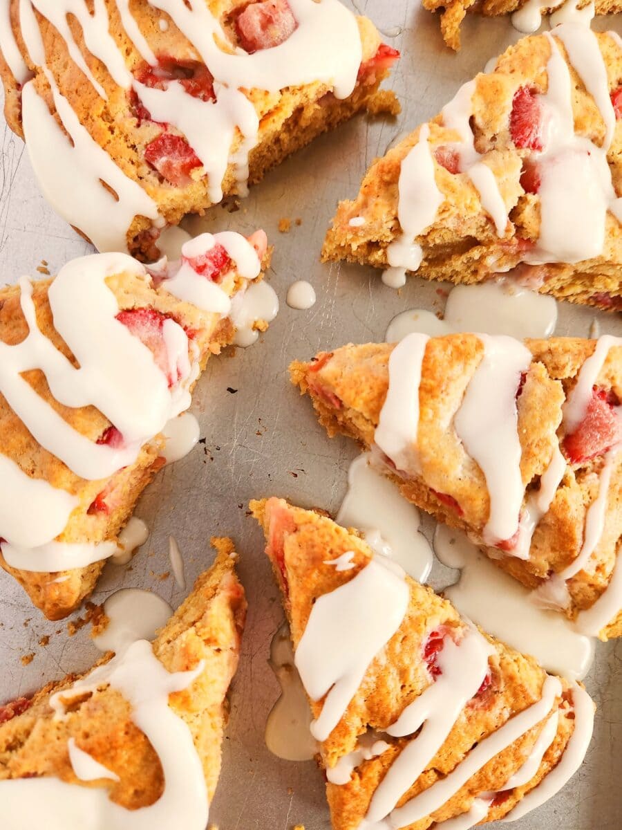 Triangular strawberry scones with white icing drizzle on a baking sheet.