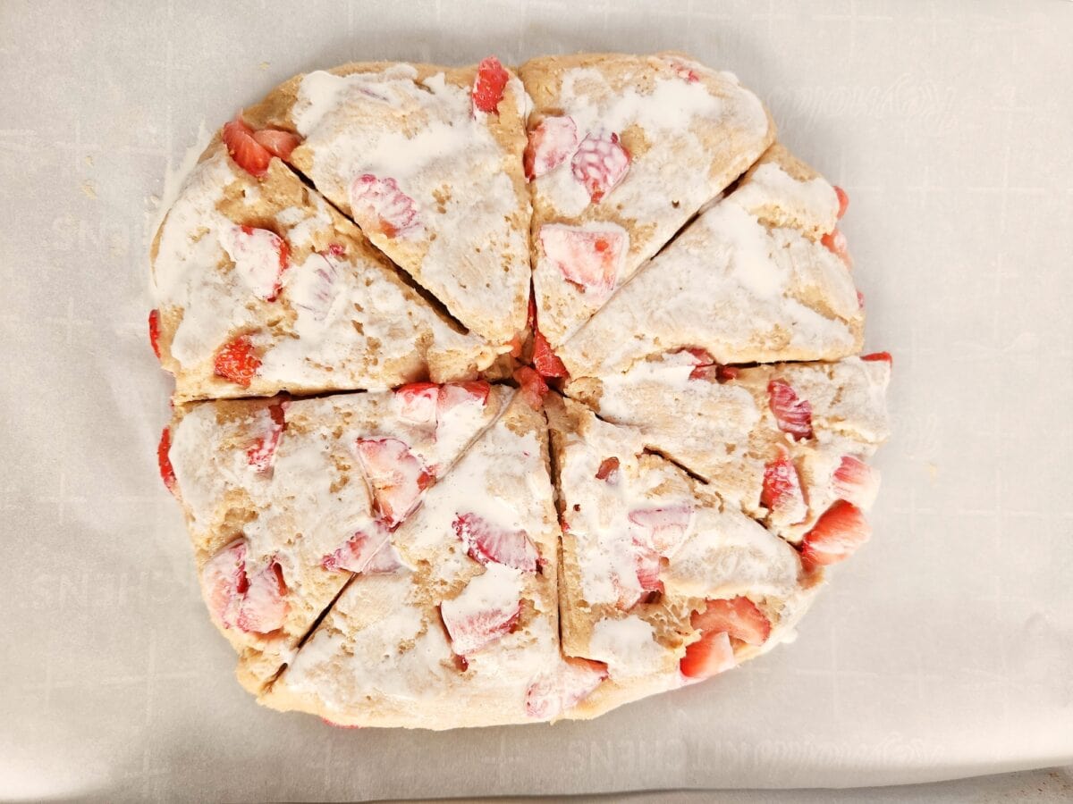 Sliced strawberry scones with icing on parchment paper.