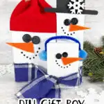 Three DIY snowmen made from gift boxes. They have button eyes, orange carrot noses, and winter accessories such as hats and scarves. Text reads "DIY Gift Box Snowmen.