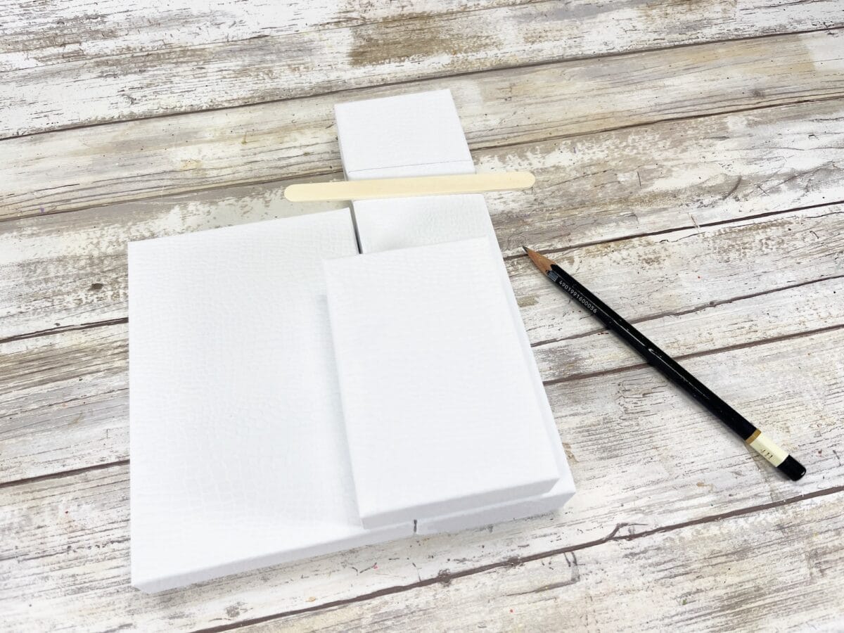 White boxes arranged with a wooden stick on top and a pencil beside them on a rustic wooden surface.