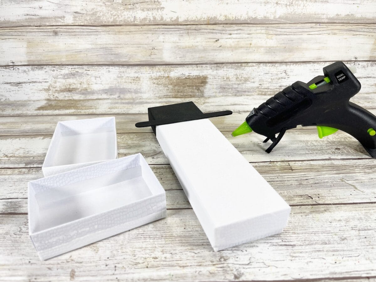 Glue gun with green tip next to white cardboard boxes on a wooden surface.