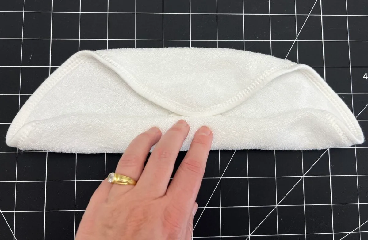 A hand with a ring holds a neatly folded white cloth on a black and white grid-patterned surface.