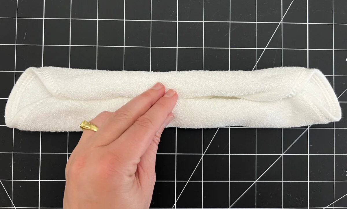 Hand with a ring holding a neatly rolled white towel on a black grid-patterned surface.