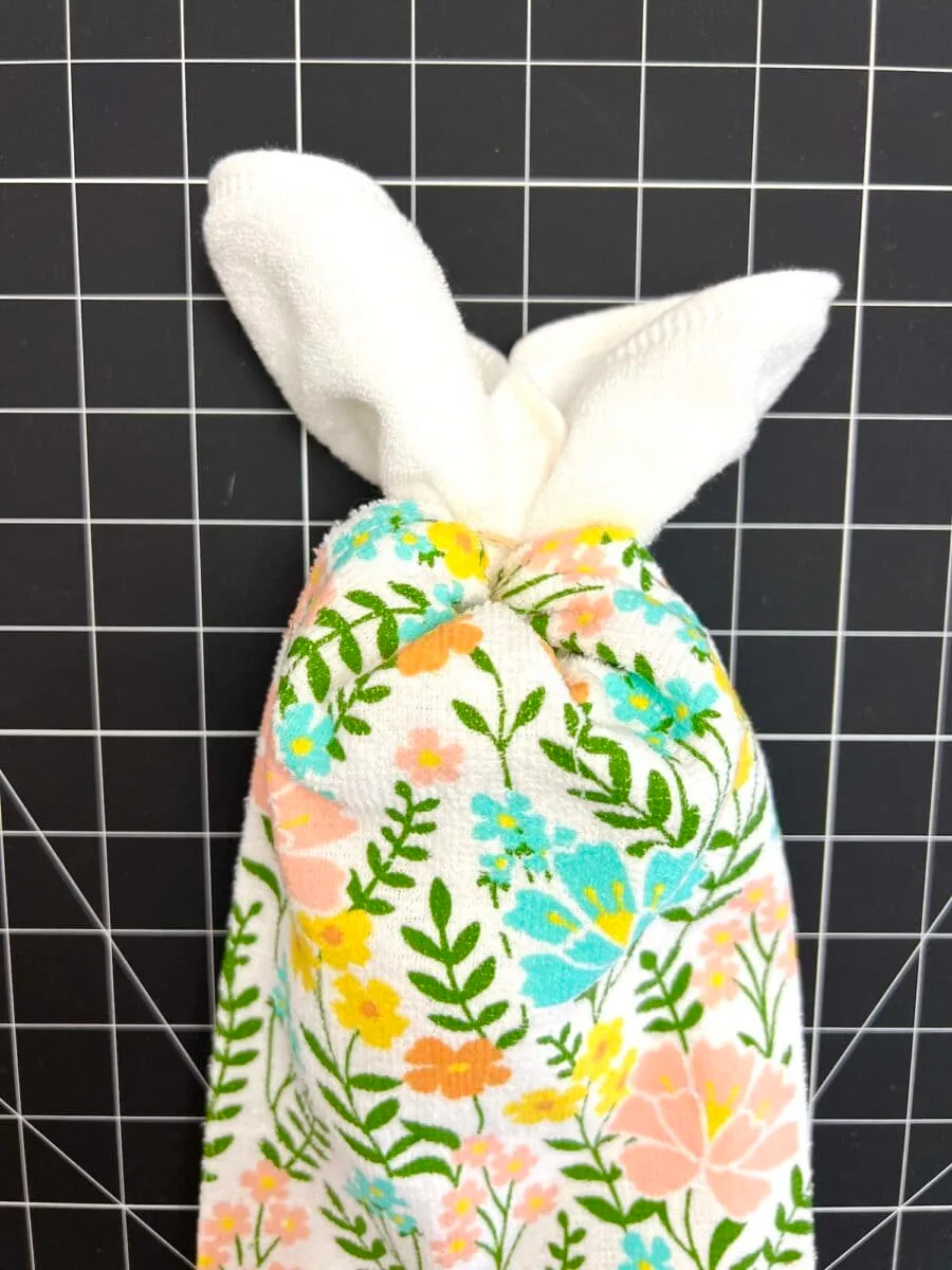 A floral towel folded into the shape of a rabbit with white ears, placed on a grid background.