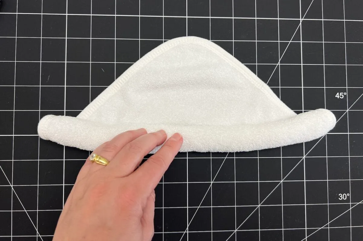 A hand with a ring holds a folded white towel against a black grid cutting mat.