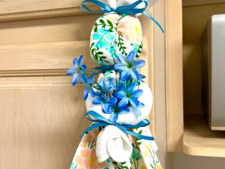 A charming dish towel, shaped like a bunny and adorned with blue flowers and a floral print, hangs gracefully on the cabinet handle.