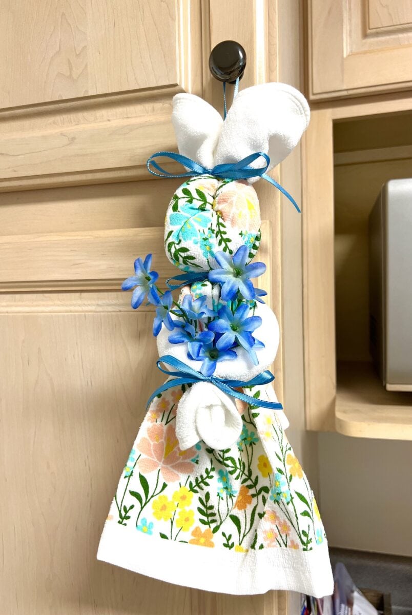 A charming dish towel, shaped like a bunny and adorned with blue flowers and a floral print, hangs gracefully on the cabinet handle.