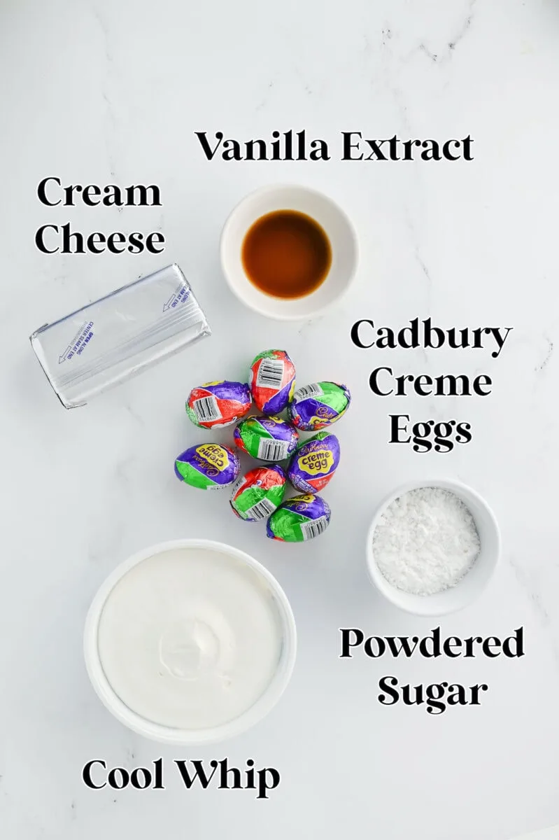 Ingredients on a countertop: cream cheese, vanilla extract, Cadbury Creme Eggs, powdered sugar, and Cool Whip.